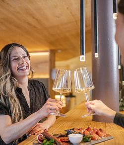 Zwei Frauen trinken ein Glas Weißwein, auf dem Tisch vor ihnen befindet sich eine Speckplatte